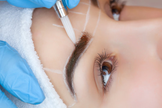 Permanent make-up for eyebrows of beautiful woman with thick brows in beauty salon. Closeup beautician doing  tattooing eyebrow.