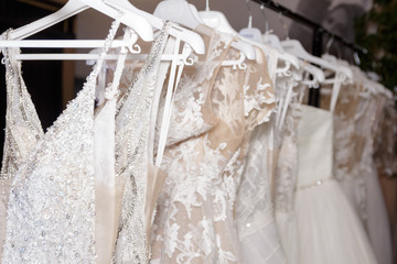 White modern lace wedding dresses hang in the store. Selective focus, close-up