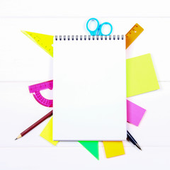 A blank notebook page surrounded by stationery on a white wooden table. Copy the space.