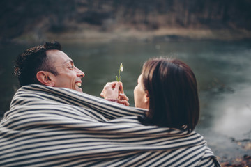 Couple covered with blanket sitting by the lake