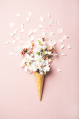 Naklejka premium Flat-lay słodki stożek wafel z białymi kwiatami migdałów na pastelowym jasnoróżowym tle, widok z góry. Koncepcja nastroju na wiosnę lub lato