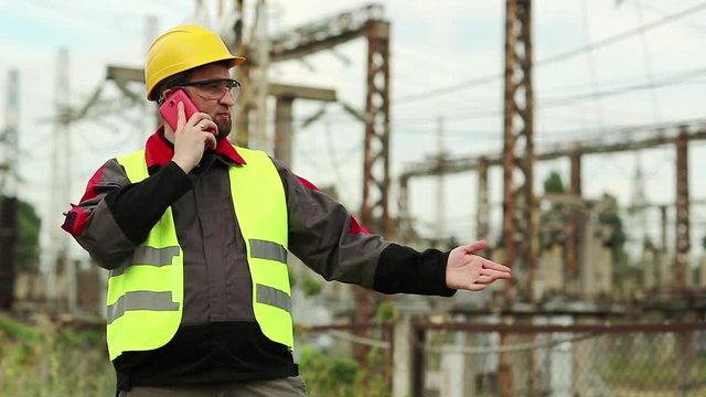 Worker on electric power plant speaks on smartphone. Power engineering specialist with cell phone on electric power station
