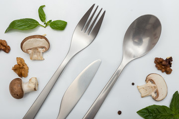 Metal inox cutlery with mushrooms, papper and basil on light gray table