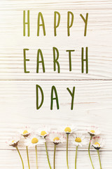 happy earth day text sign on beautiful daisy flowers on rustic white wooden background top view. greeting card. environmental concept. earth day. save environment. eco