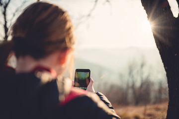 Girl taking photos with smart phone in forest