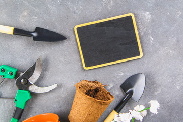 Garden tools and pots on a gray concrete background. Chalk board. Top view, copy space.