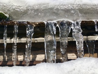 eiszapfen in einer reihe von einem schneebedeckten dach hängend/wasser zu eis gefroren, gebilde in der natur/kalte winterzeit, starre strukturen
