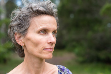 Profile of middle aged woman with grey hair against forest background (selective focus)