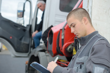 Man writing on clipboard while lorry driver waits