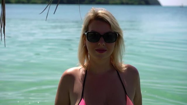 Young woman in pink bikini at the beach near palm