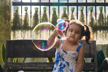 cute little girl playing soap bubbles with bubble gun on a sunny summer day.