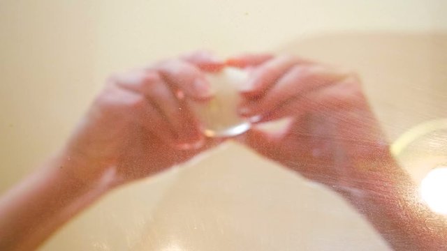 A raw egg yolk floats directly above the camera. A pair of hands - distorted by the first embryo's albumen - breaks a second egg. The ovum falls and lands by the original egg. The two yolks slide arou