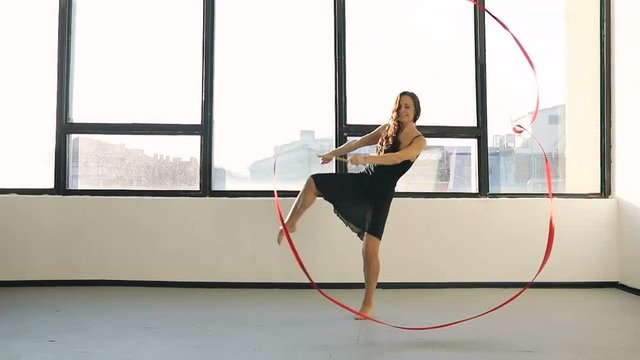 Brunette young women dance rhythmic gymnastics, modern with red ribbon in black sexy dress in front of the windows. sun shade. Super slow motion. 120 fps.