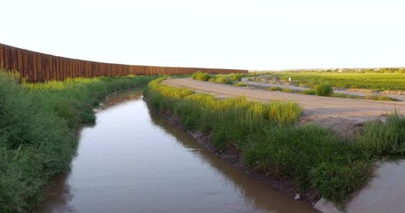 A muddy river moves slowly next to the fence separating the borderline between America and Mexico. The wall and water prevent illegal emigration and aliens from crossing the border between the two cou