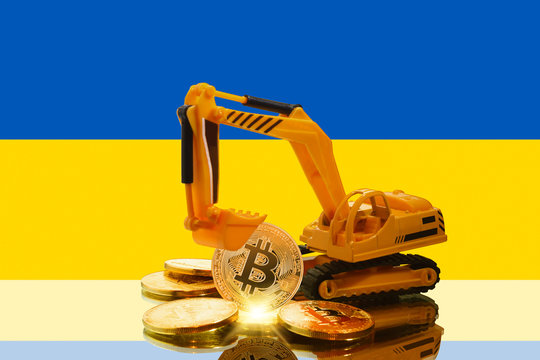 bitcoin mining concept; miniature Excavator and Bitcoin coins (physical version) against the background of the flag of Ukraine