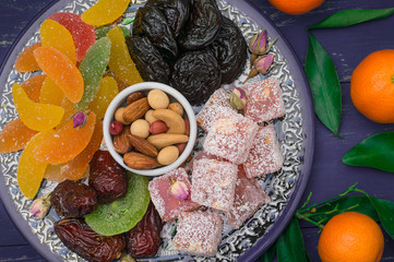 Set of eastern desserts. Marmalade, kivi, prunes, rahat lokum, nuts, mandarin, persimmon, dried apricots, pistachios, dates, raisins in a colorful blue plate. Wooden rustic background. Top view