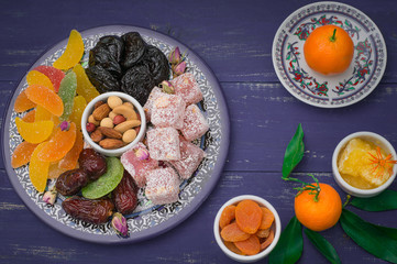 Set of eastern desserts. Marmalade, kivi, prunes, rahat lokum, nuts, mandarin, persimmon, dried apricots, pistachios, dates, raisins in a colorful blue plate. Wooden rustic background. Top view