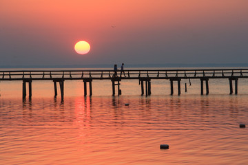 Obraz premium A couple walking down a long pier with the dropping sun in the background.