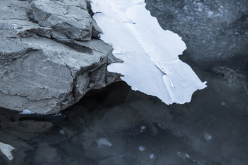 close up on rocks surrounded by frozen ice plaques in winter season lake