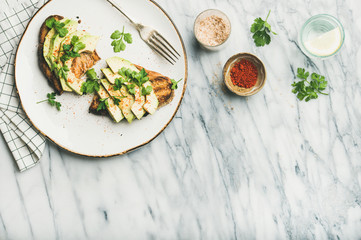 Healthy vegan breakfast or lunch. Flat-lay of avocado toast on plate with seasoning and glass of lemon water over marble background, top view, copy space. Clean eating, detox, dieting food concept