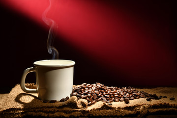 Cup of coffee with smoke and coffee beans on reddish brown background