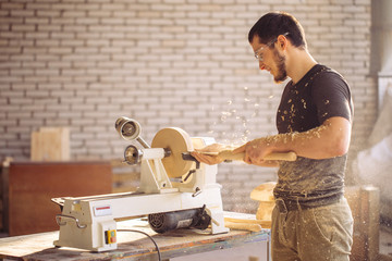 Young carpenter processing wooden plank on special woodworking machine