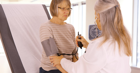 A elderly patient gets her blood pressure checked by her doctor. An older doctor takes a patients blood pressure