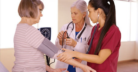 Fototapeta premium A patient gets her blood pressure taken by a doctor and a nurse. Two medical professionals take the blood pressure from their elderly patient