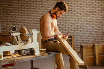 naked carpenter using straightedge to draw line on board.