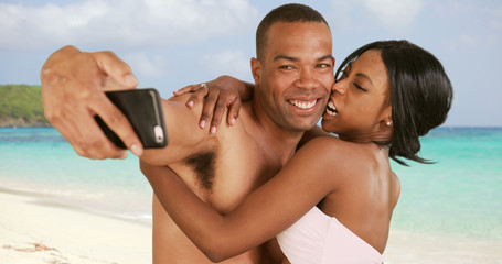 Fototapeta premium Engaged couple on honeymoon taking selfies on Caribbean beach. Man and woman with smartphone being silly and playful