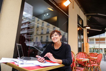 middle aged female student using laptop for writing a research work. Woman sitting at red table in...
