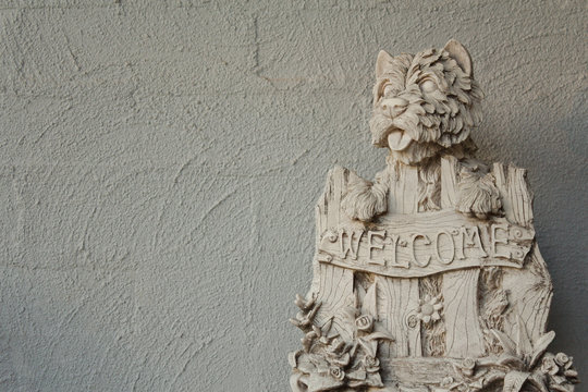 A West Highland Terrier Stone look garden ornament with a "Welcome" sign against a grey brick background.