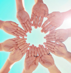 overhead view of a group of people making a circle shape with their hands directly below the sun with a lens flare toned with a retro vintage instagram filter