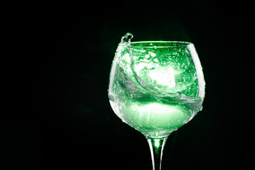 Splashing water in the wine glass with green background