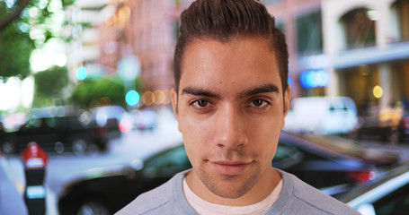 Wide angle close up shot of Hispanic man standing outside on street looking at camera. Portrait closeup of Latino millennial making eye contact