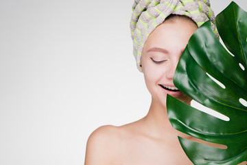 young happy girl with a towel on her head holds a green leaf in her hands, enjoying spa treatments