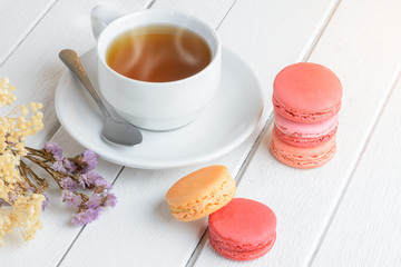 Different types color of macaroons with Cup of hot tea on white wooden background