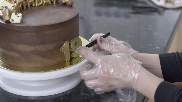 Confectioner in gloves makes a cake to 19th anniversary of birthday. Close-up on order in confectionery hand make a dessert with letters of happy birthday, date and candy. slowmotion slow motion