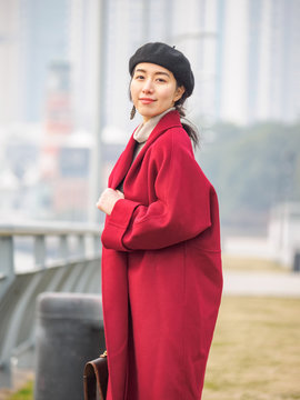 Beautiful young brunette woman in red coat with beret hat. Outdoor fashion portrait of glamour young Chinese cheerful stylish lady. Emotions, people, beauty and lifestyle concept.