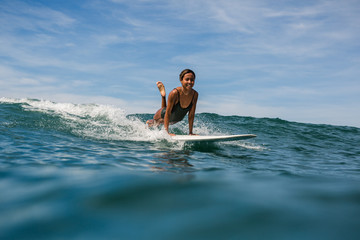 Beautiful young indonesian woman in bikini surfing wave in Bali on the background of blue sky,...