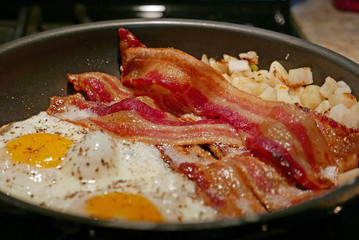 Amerikanisches Frühstück mit zwei Spiegeleiern, Schinkenspeck und Bratkartoffeln in Bratpfanne