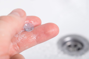the lens lies in the soap solution on the fingers on the background of the wash basin, close-up
