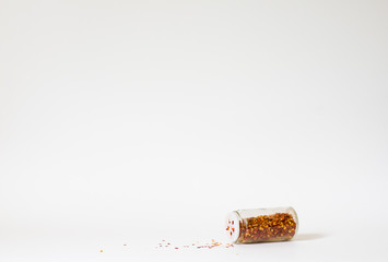 Chili jar toppled with sprinkles on white background