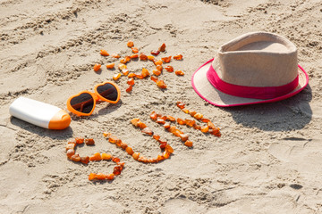 Obraz premium Word and shape of sun, sunglasses, sun lotion and straw hat on sand at beach, summer time concept