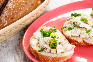 Slice of baguette with fish paste on plate and fresh rolls in background