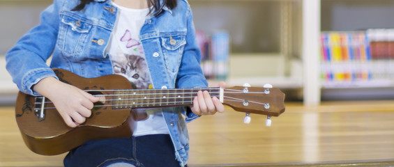 Little child playing ukulele in the library bossanova music in summer time, Cute girl play guitar vintage style, hand picking Guitar ,Ukulele on the library .