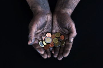 Dirty male hands of a worker keep the euro and euro cents on a dark background. Low-paid work. Money in the hands of a beggar. Low salary.