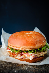 homemade chicken burger, packed in paper, on a wooden table on a dark background