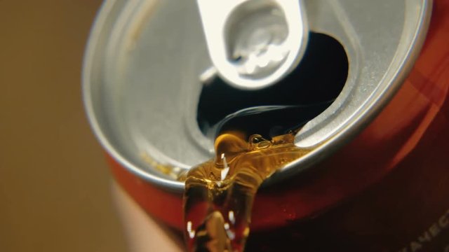 Soda is poured from a can of red color against a dark background. Slow-motion close-up shooting