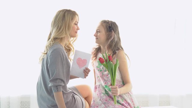 Daughter gave her mother a bouquet of tulips and a postcard made by own hands.